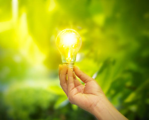 hand holding a light bulb with energy on fresh green nature back
